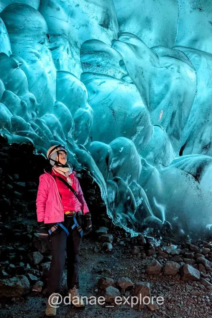 Me, wearing a pink shirt and helmet, observing the blue interior of the ice cave in Vatnajökull.