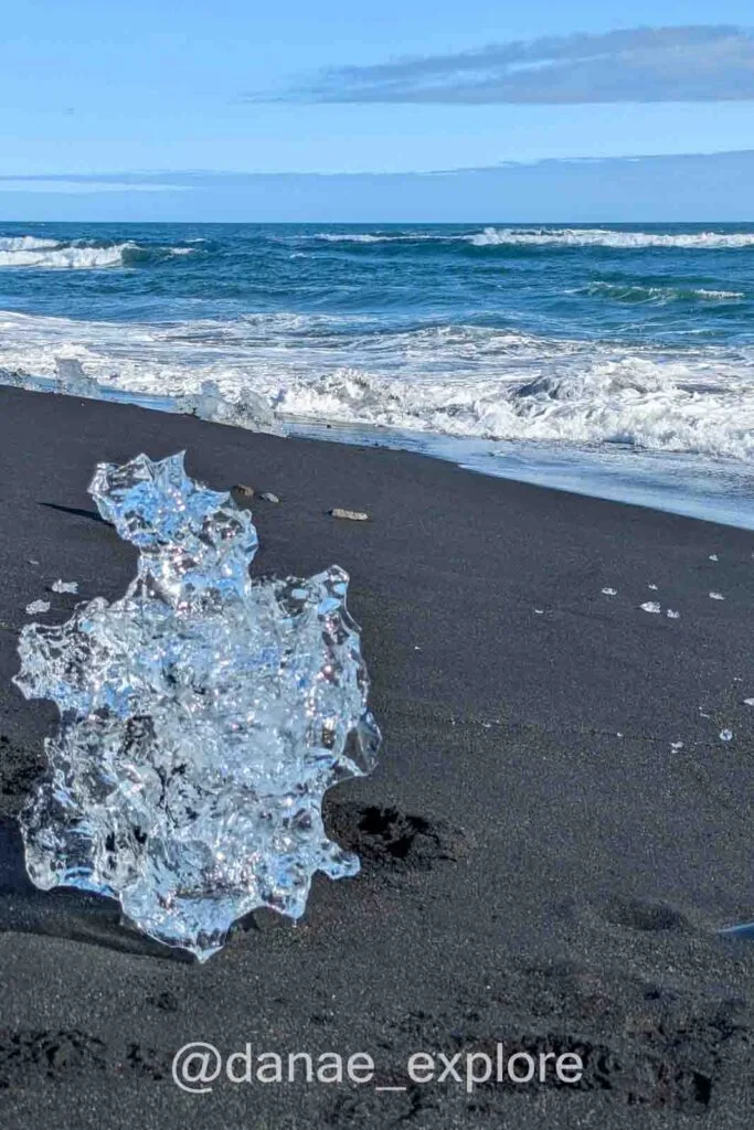 Diamond Beach, the famous Icelandic beach with icebergs. The photo shows a piece of transparent ice on the black sand, with the Atlantic waves in the background.