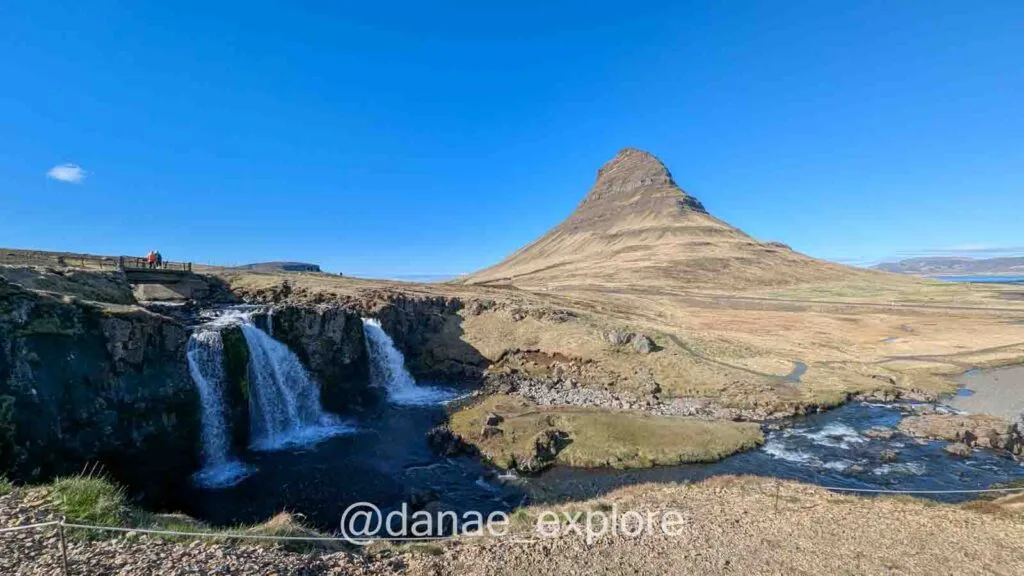 Kirkjufell mountain with Kirkjufellsfoss waterfall in the foreground, one of the most famous sights to see in Iceland. It's a sunny day with clear skies and no clouds.