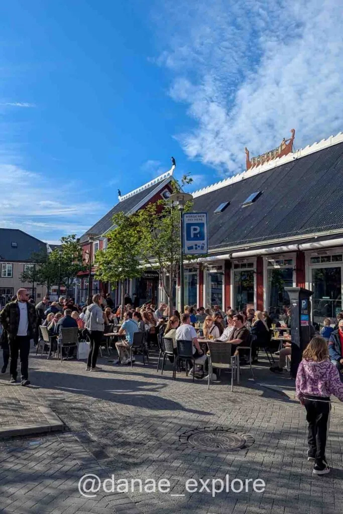 Busy street with outdoor tables and locals enjoying the sun in Reykjavík.