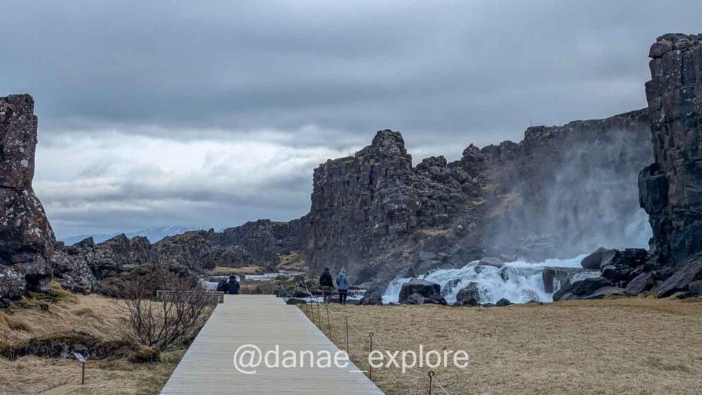 Cachoeira Öxarárfoss cercada por paredões de pedra da divisa das placas continentais no Parque Nacional Þingvellir, com passarela de madeira