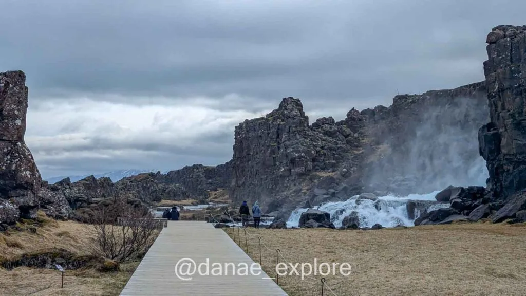 Öxarárfoss waterfall surrounded by rock walls marking the boundary between continental plates in Þingvellir National Park, with a wooden walkway.