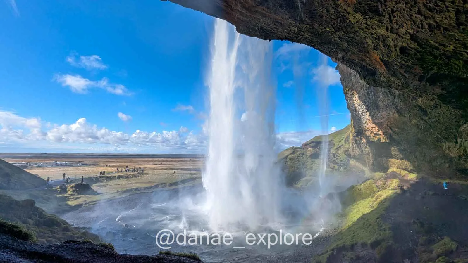 Vista por trás da cachoeira Seljalandsfoss, com a água caindo diante do campo aberto, uma das coisas mais legais para se fazer na Islândia