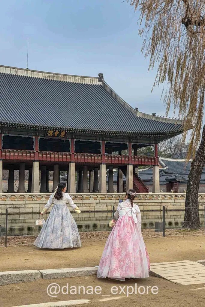 Visitantes com hanbok no Palácio Gyeongbokgung em Seul diante de pavilhão tradicional e lago