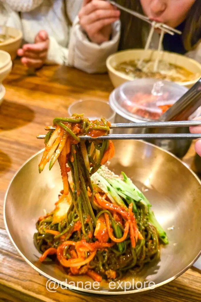 Prato de bibim guksu com kimchi sendo servido com hashis em restaurante típico na Coreia do Sul