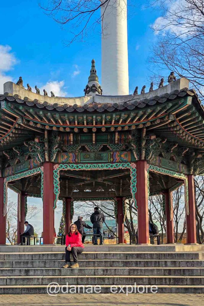 Eu sentada nos degraus de pavilhão tradicional coreano, ao lado da N-Seoul Tower