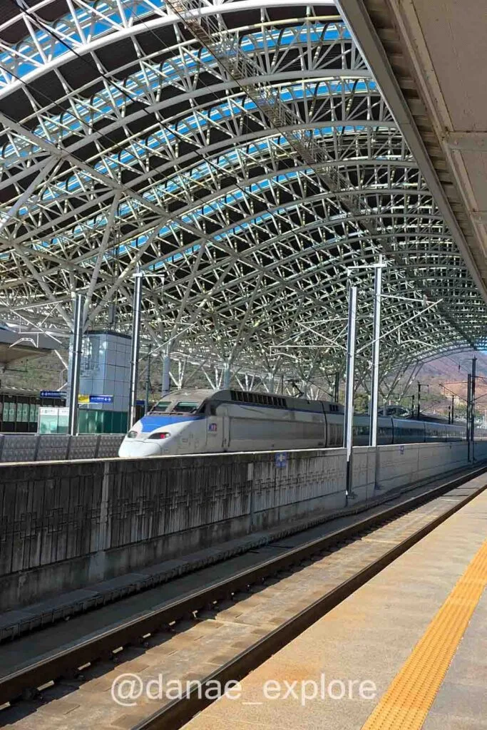Trem KTX em estação moderna na Coreia do Sul com estrutura metálica e trilhos amplos
