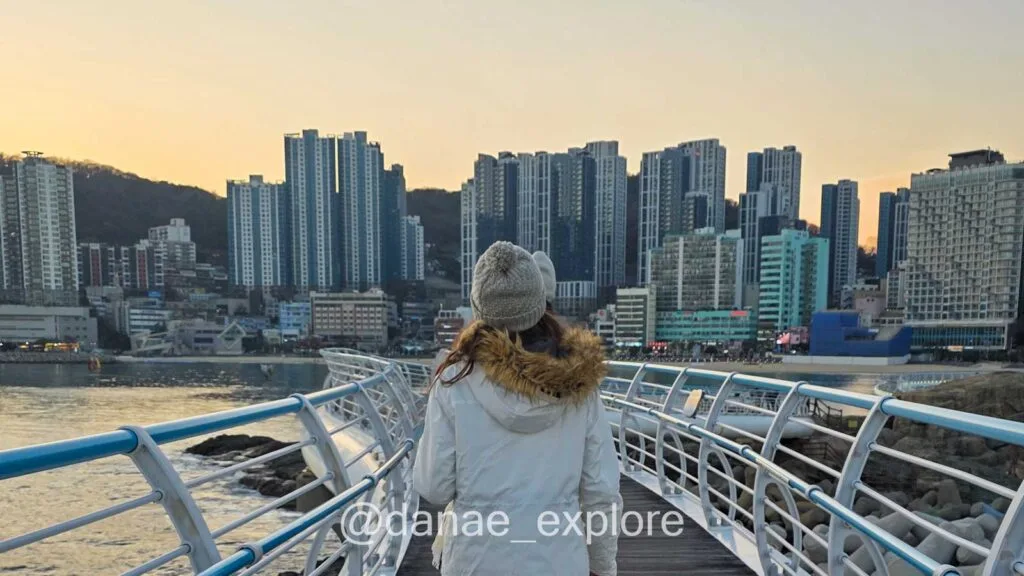 Passarela em Busan à beira-mar com vista para prédios e litoral ao entardecer