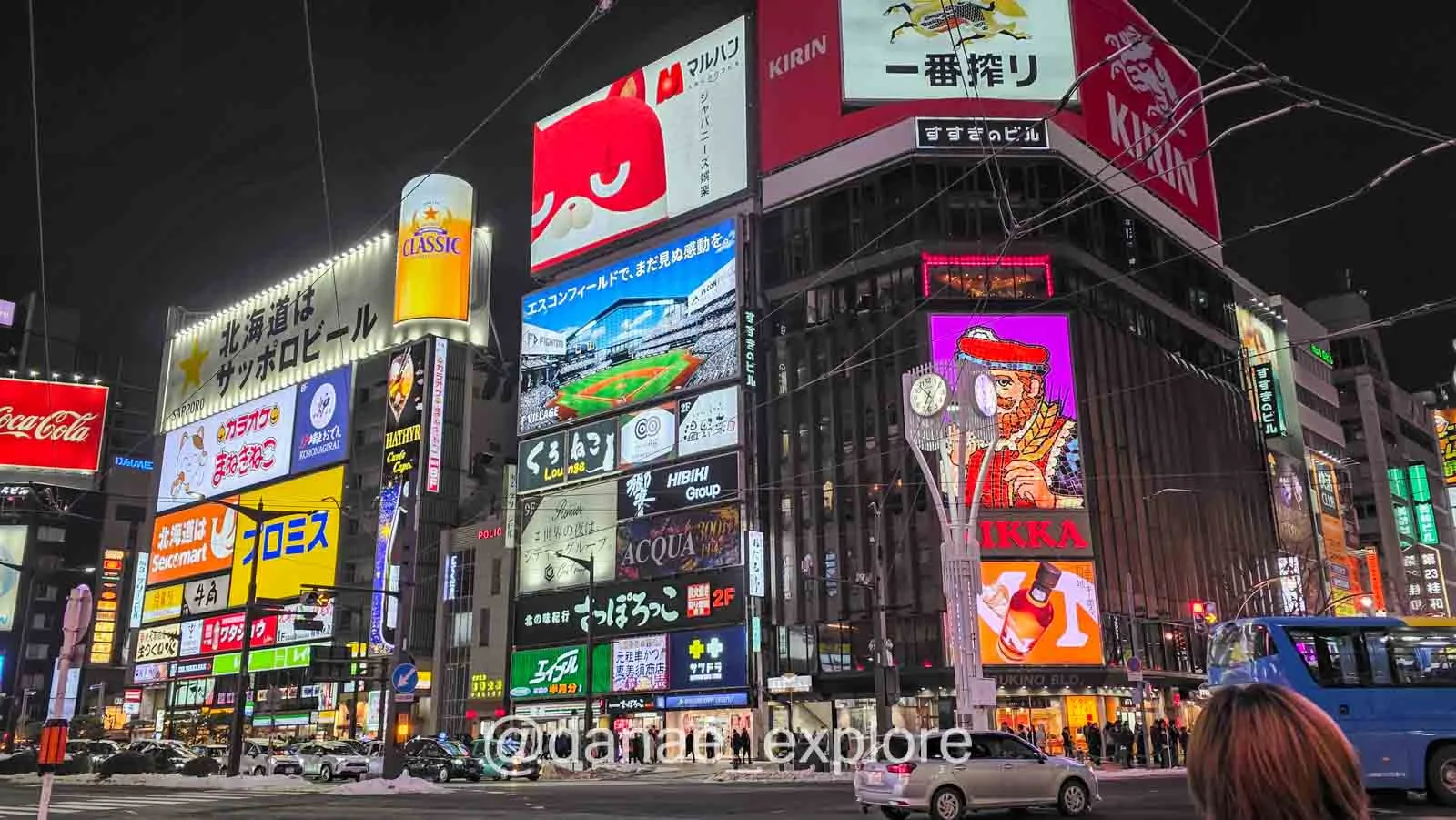 Vista urbana noturna de Sapporo com neve nas ruas e letrieros luminosos nos prédios, com desaque para o Nikka Sign