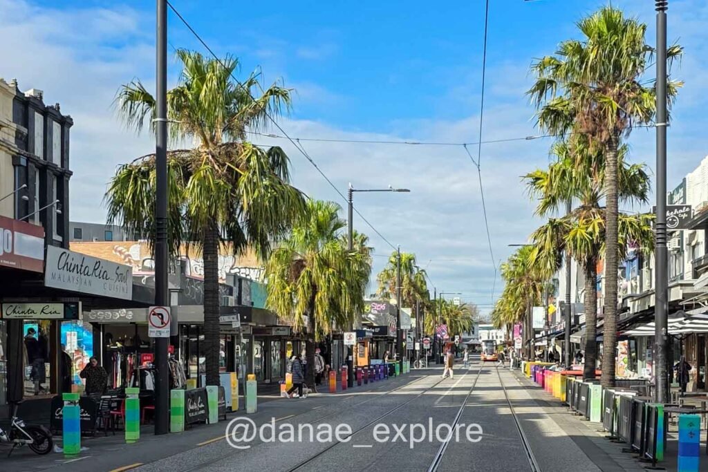 Acland Street, com palmeiras nas calçadas, onde fica o agito de St. Kilda, com lojas, bares e restaurantes.