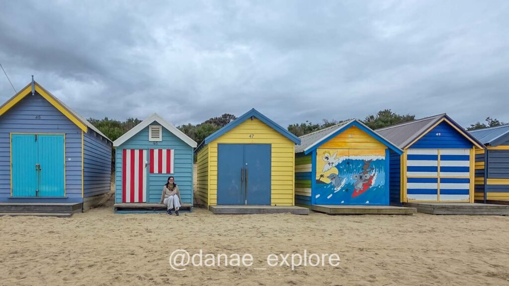 Eu sentada em frente as Brighton Bathing Boxes, na praia de Brighton em Melbourne
