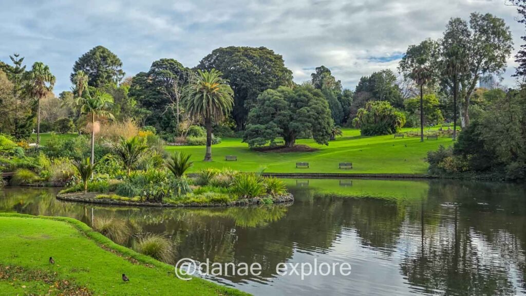 Jardim Botânico de Victoria, em Melbourne: há um lago com uma pequena ilha em primeiro plano e gramado e vegetação ao fundo, em um dia nublado.