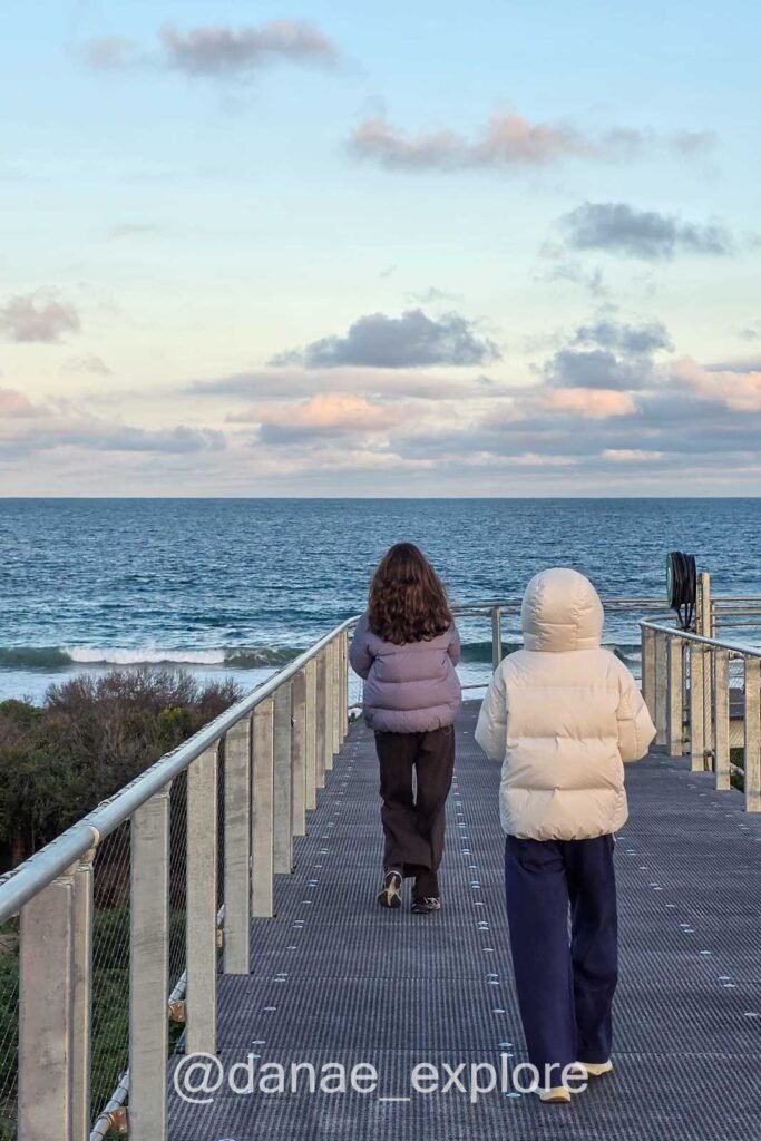 Duas meninas caminhando ao pôr do sol em passarelas que levam ao local de observação dos pinguins pequenos na Ilha Phillip