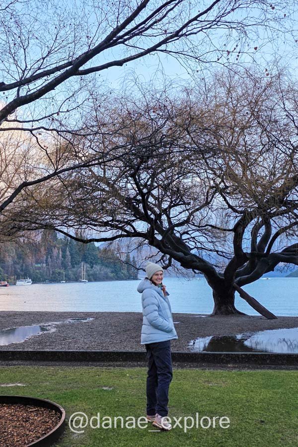 Eu no Queenstown Gardens, sob uma árvore de galhos sem folhas.