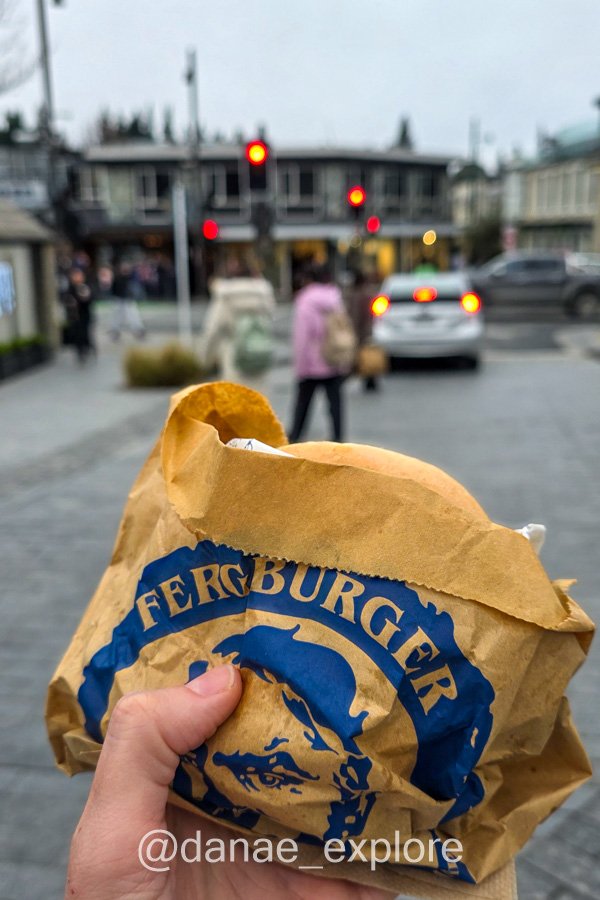 Mão segura um pacote de hambúrguer do Fergburger em uma rua de Queenstown.