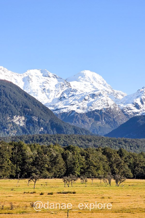 Campo verde e floresta diante de dois picos cobertos de neve na região de Glenorchy, próximo a Queenstown