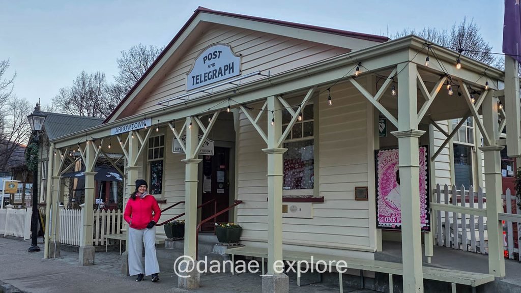Eu passeando em Arrowtown, na foto estou de blusa vermelha e calça branca diante do antigo prédio dos correios e telégrafos de Arrowtown.