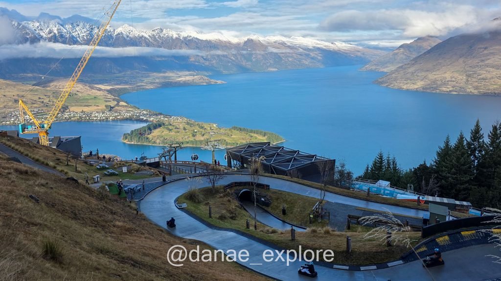 Carrinhos descem a pista do Skyline Luge, com o Lago Wakatipu e montanhas nevadas ao fundo