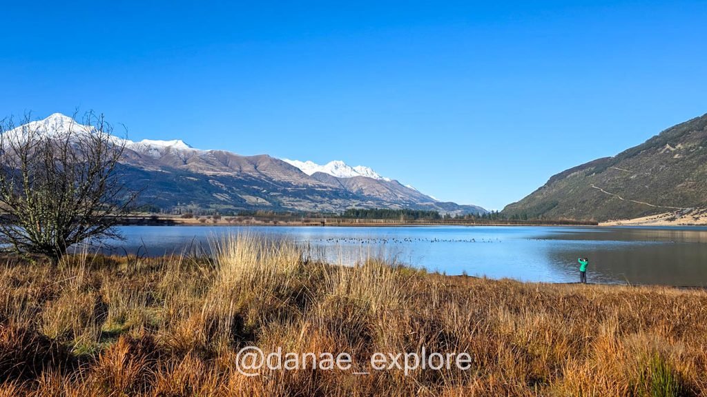 Lagoa cercada por vegetação dourada em Glenorchy, com montanhas nevadas ao fundo.
