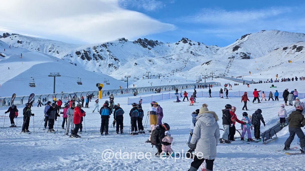 Esquiadores e iniciantes na neve em The Remarkables, com teleféricos e pistas ao fundo.